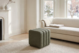 Abbadia ottoman in moss on an ivory wool rug in front of an ivory boucle sofa in a Toronto living room with a white fireplace