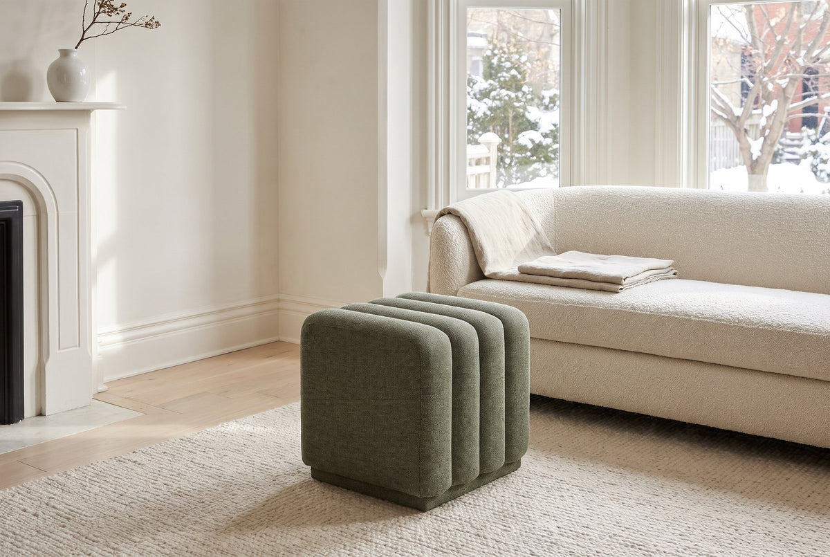Abbadia ottoman in moss on an ivory wool rug in front of an ivory boucle sofa in a Toronto living room with a white fireplace