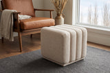 Abbadia ottoman in oat on a charcoal wool rug beside a cognac leather lounge chair in a Calgary living room