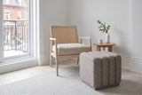 Abbadia ottoman in stone on a light grey rug beside a cane armchair in a Montreal Plateau reading corner