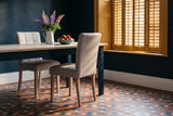 Two light grey Adelina upholstered dining chairs with pale oak legs at a pine table with ink-blue legs, a white jug of purple and pink lupins and a green bowl of nectarines, in an ink-blue room with closed mustard shutters and a patterned cement tile floor