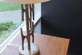 Adeline lamp on a wood side table by a window, showing its branching brass stem