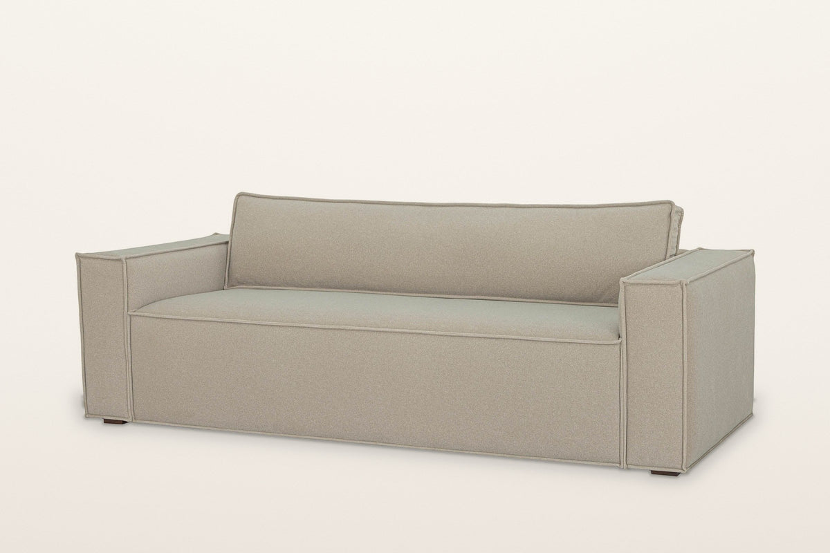 Agerola track arm sofa in Sand fabric, three-quarter view on a warm white studio backdrop: wide square arms, one long seat and one long back cushion, flange seams