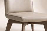 Close-up of one beige Aileen leather dining chair on an off-white backdrop: the pebble-grain leather back and seat, the self-colour piping along the edges, the ash underframe and the tops of the splayed legs