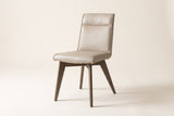 Three-quarter view of one beige Aileen leather dining chair on an off-white backdrop, with the one-piece leather seat and back, the seam across the top band, the self-colour piping and four splayed tapered ash legs