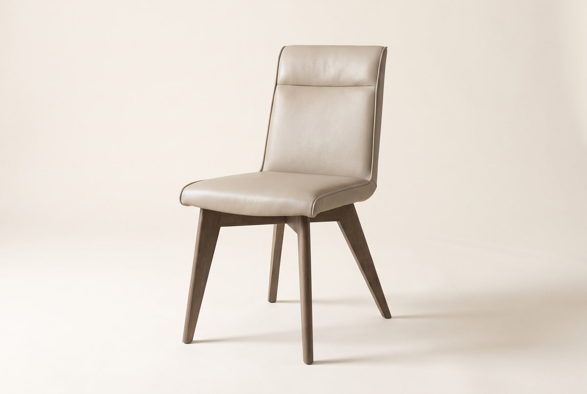 Three-quarter view of one beige Aileen leather dining chair on an off-white backdrop, with the one-piece leather seat and back, the seam across the top band, the self-colour piping and four splayed tapered ash legs