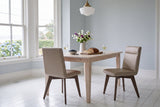 Two beige Aileen leather dining chairs at a pale wood table with sweet peas in a jug, bread, cheese, blueberries and white wine, in a pale blue room with white sash bay windows and hydrangeas outside, in a Victorian house in the South End of Halifax