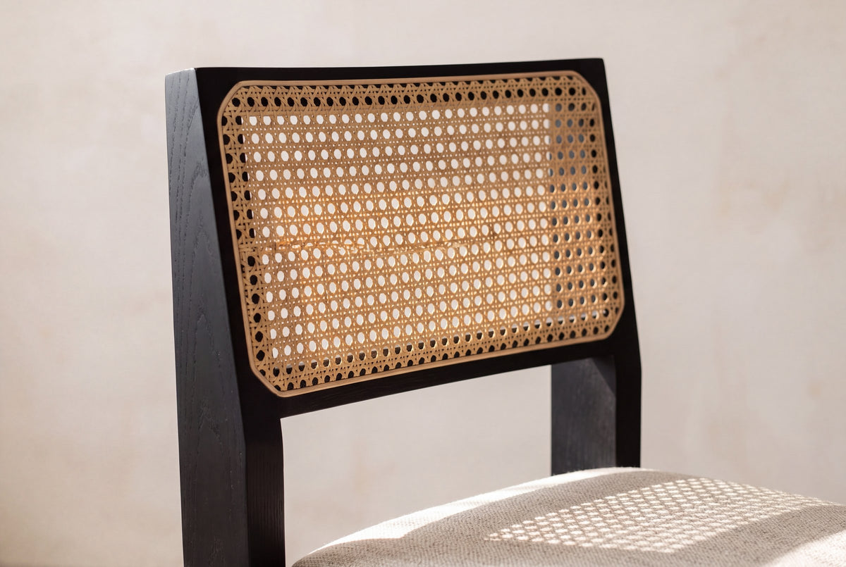Close-up of the Alaya chair's natural cane back in its black oak frame, with sunlight passing through the weave