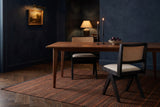 Two Alaya black oak dining chairs with cane backs and oatmeal seats at a walnut table with lit candles and a bowl of plums, in a midnight-blue room with a lit oil painting and a striped rug