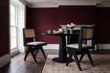 Two Alaya cane dining chairs at a round black table in a London townhouse with oxblood walls
