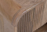 Close-up of the Alberona corner in natural: the rounded bend over the reeded drawer front, pale solid mango grain