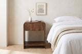Alberona nightstand in walnut beside a white bed in a Muskoka cottage bedroom, a white bud vase with dried grasses on top