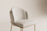 Close-up of the Alexander chair layered ivory fabric back, padded seat and brass rail on an off-white backdrop