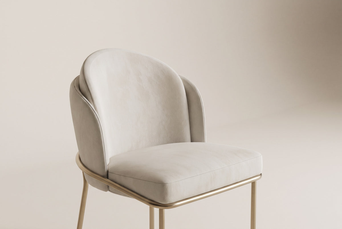Close-up of the Alexander chair layered ivory fabric back, padded seat and brass rail on an off-white backdrop