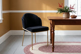 Black velvet dining chair with brass legs beside the end of a cherry farm table in a mustard-walled winter dining room, evergreen and winterberry branches in a stoneware crock