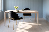 Two Alexander black velvet dining chairs with brass legs at a pale ash table with celadon cups and white tulips, against powder blue-grey panelled walls in morning light