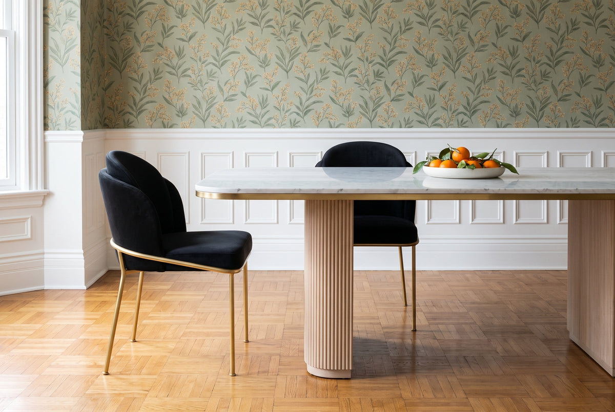 Two Alexander black velvet dining chairs with brass legs at a white marble table on a fluted oak base, with a dish of clementines, botanical wallpaper and a white wainscot