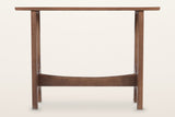 Amelia console table in walnut, straight front view: a thin top on two slotted trestles joined by a curved stretcher