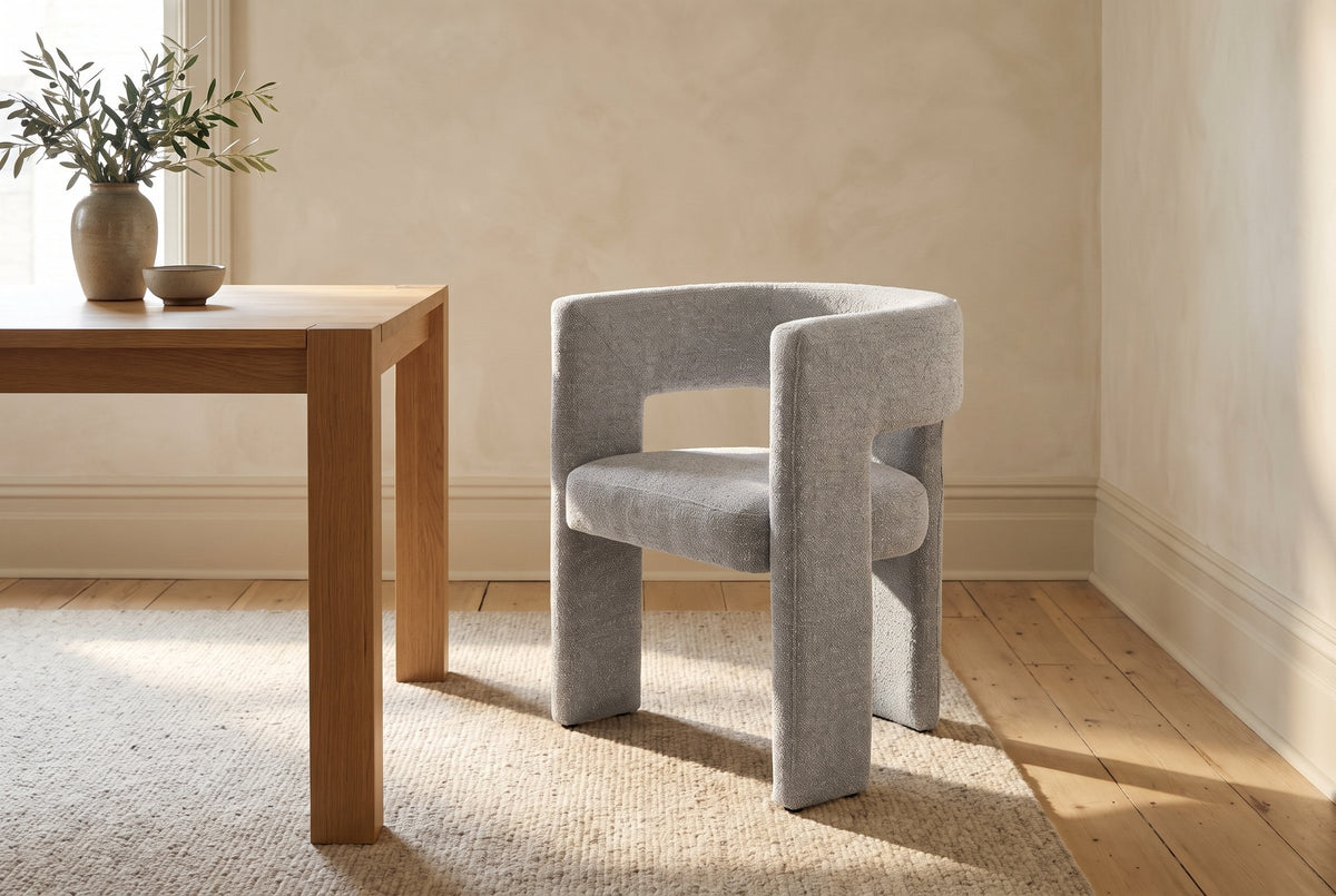 Andrea light grey woven fabric dining chair at the end of a solid oak table, with olive branches in a vase
