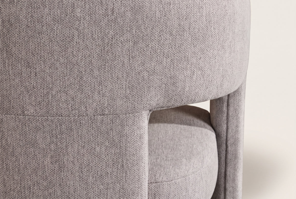 Close-up of the Andrea chair back band and wide rear slab leg in light grey woven fabric on an off-white backdrop
