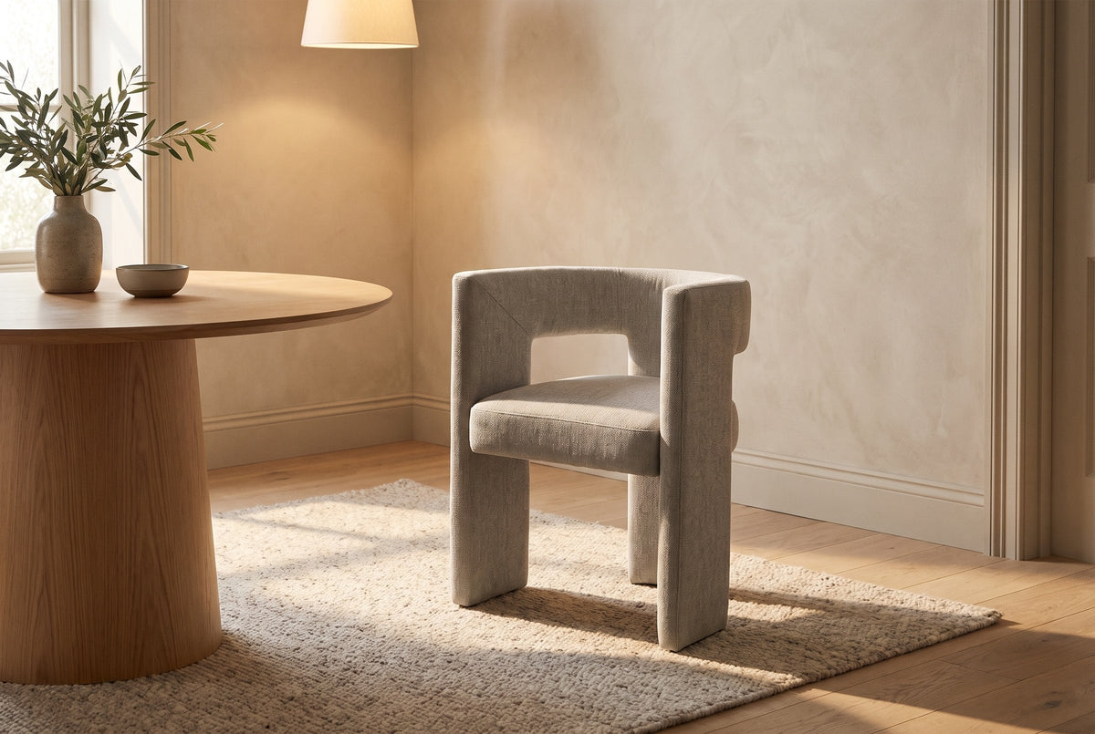Andrea light grey woven fabric dining chair beside a round oak pedestal table under a linen pendant in warm evening light