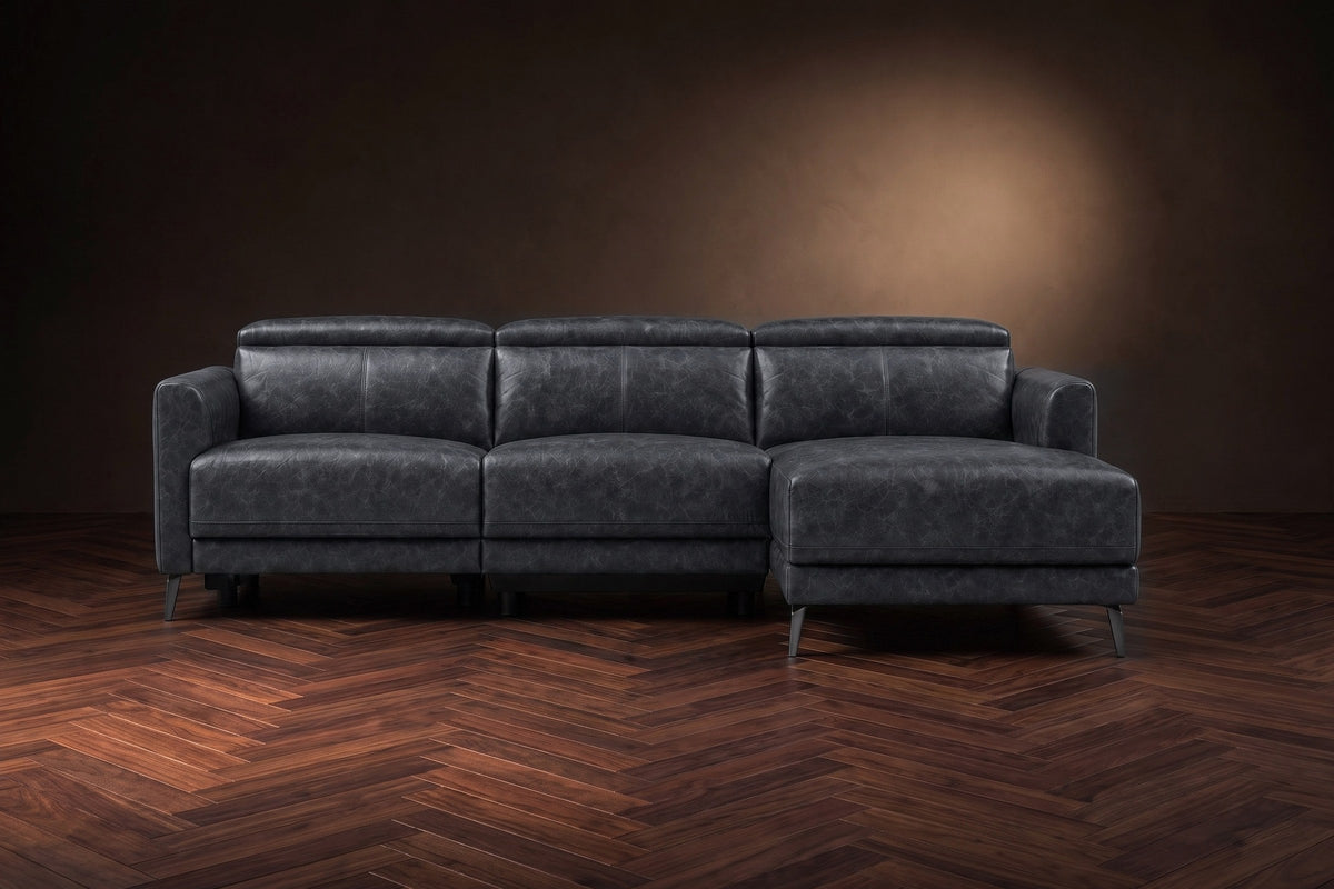 The Andria distressed leather reclining sectional seen from the front on a walnut herringbone floor, headrests down and the footrest closed. Shown in Aged Slate, Right chaise.