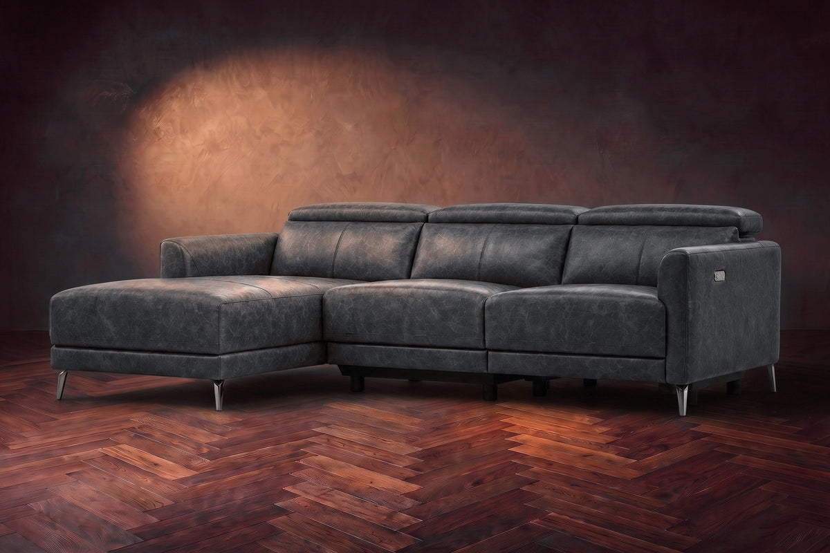 The Andria distressed Italian leather power reclining sectional on a walnut herringbone floor against a brown plaster wall, three-quarter view, headrests down and the footrest closed. Shown in Aged Slate, Left chaise.
