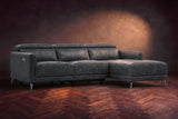 The Andria distressed Italian leather power reclining sectional on a walnut herringbone floor against a brown plaster wall, three-quarter view, headrests down and the footrest closed. Shown in Aged Slate, Right chaise.