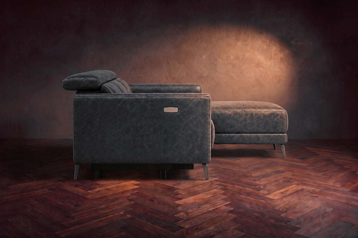 The Andria distressed leather sectional seen from its box-arm end, the chaise reaching forward, on a walnut herringbone floor. Shown in Aged Slate, Right chaise.