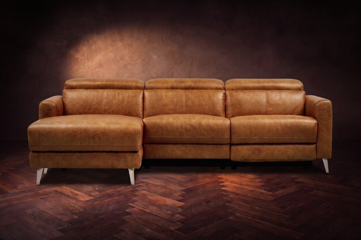 The Andria distressed leather reclining sectional seen from the front on a walnut herringbone floor, headrests down and the footrest closed. Shown in Antiqued Caramel, Left chaise.
