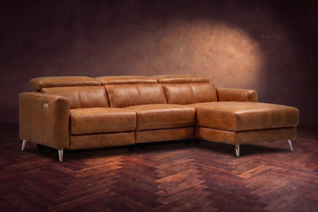 The Andria distressed Italian leather power reclining sectional on a walnut herringbone floor against a brown plaster wall, three-quarter view, headrests down and the footrest closed. Shown in Antiqued Caramel, Right chaise.