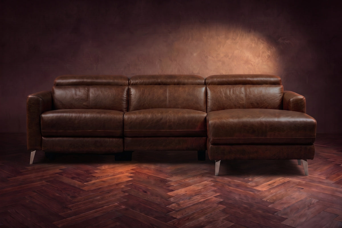 The Andria distressed leather reclining sectional seen from the front on a walnut herringbone floor, headrests down and the footrest closed. Shown in Burnished Chestnut, Right chaise.