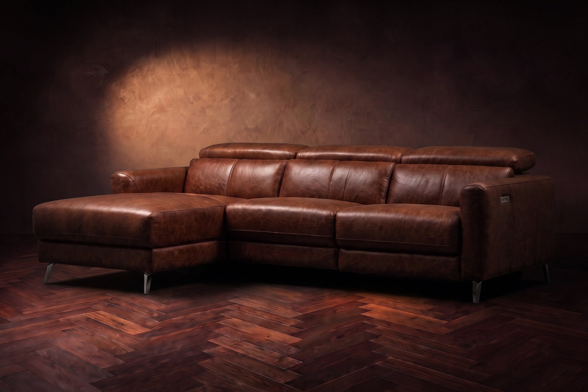 The Andria distressed Italian leather power reclining sectional on a walnut herringbone floor against a brown plaster wall, three-quarter view, headrests down and the footrest closed. Shown in Burnished Chestnut, Left chaise.