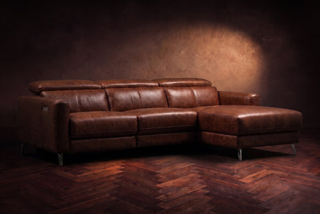 The Andria distressed Italian leather power reclining sectional on a walnut herringbone floor against a brown plaster wall, three-quarter view, headrests down and the footrest closed. Shown in Burnished Chestnut, Right chaise.