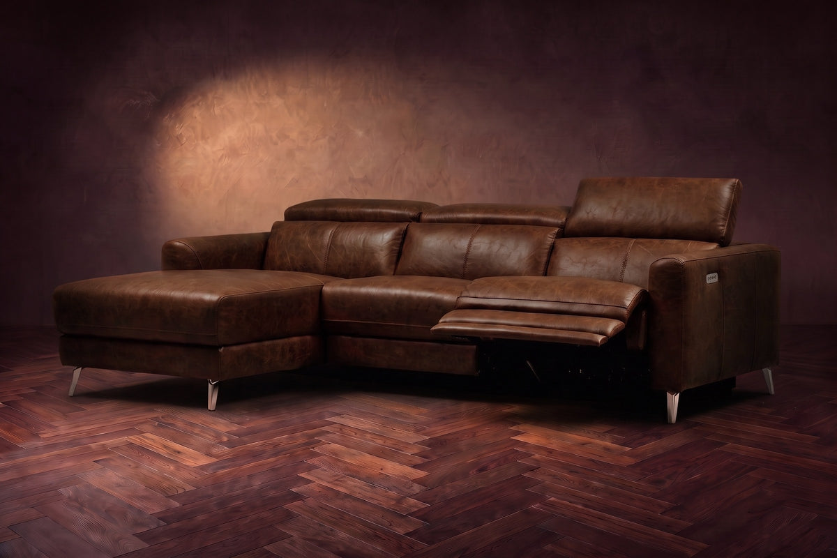 The Andria power reclining sectional on a walnut herringbone floor with the arm-end power recliner open: its two-tier footrest out and its headrest raised. Shown in Burnished Chestnut, Left chaise.