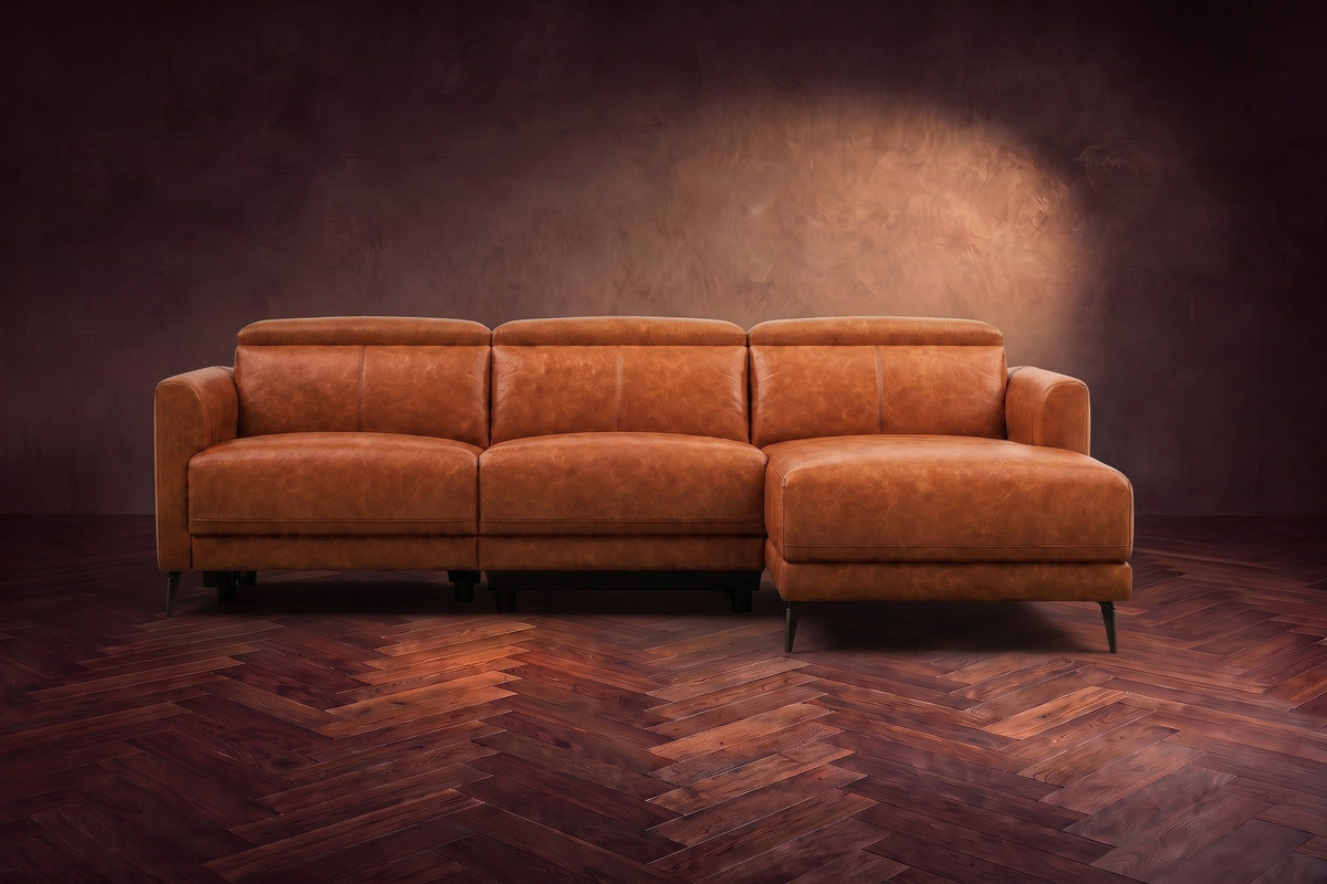 The Andria distressed leather reclining sectional seen from the front on a walnut herringbone floor, headrests down and the footrest closed. Shown in Tuscan Cognac, Right chaise.