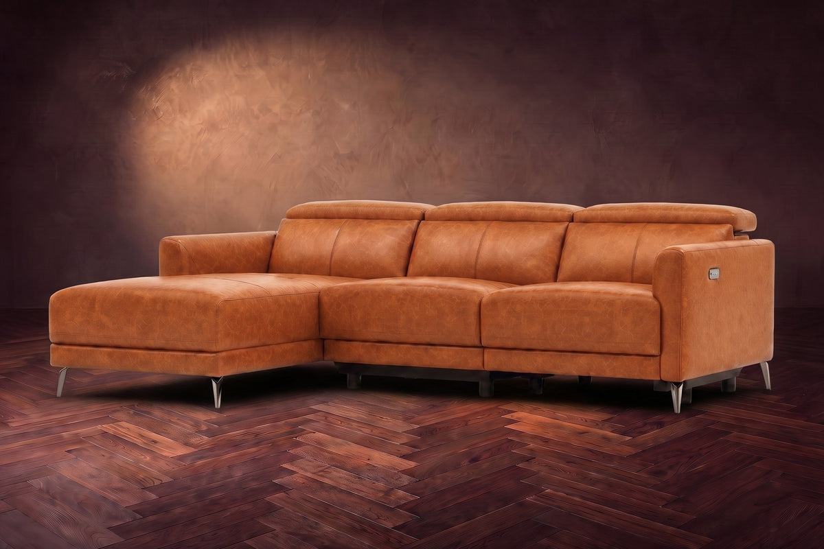The Andria distressed Italian leather power reclining sectional on a walnut herringbone floor against a brown plaster wall, three-quarter view, headrests down and the footrest closed. Shown in Tuscan Cognac, Left chaise.