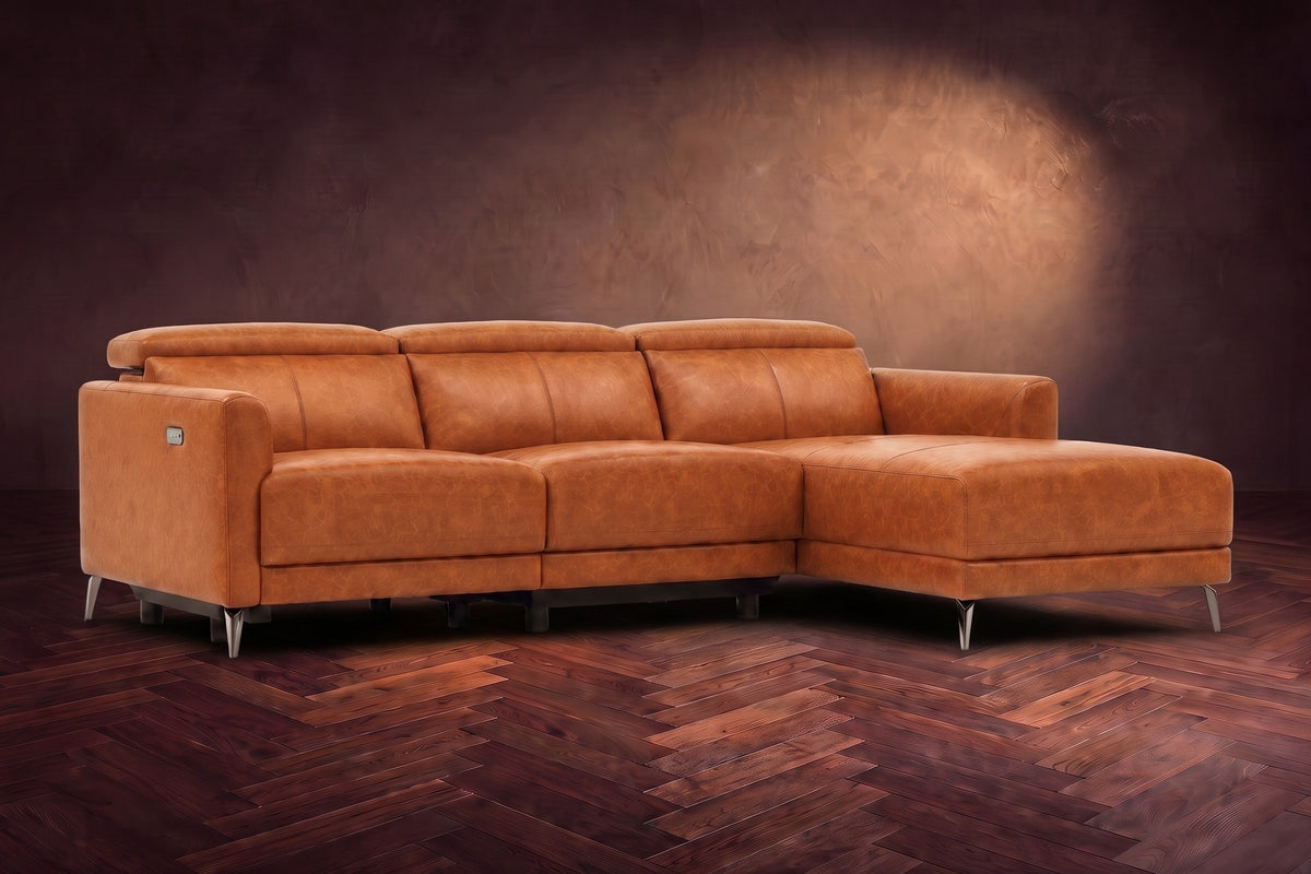 The Andria distressed Italian leather power reclining sectional on a walnut herringbone floor against a brown plaster wall, three-quarter view, headrests down and the footrest closed. Shown in Tuscan Cognac, Right chaise.