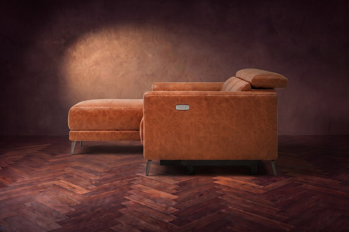 The Andria distressed leather sectional seen from its box-arm end, the chaise reaching forward, on a walnut herringbone floor. Shown in Tuscan Cognac, Left chaise.