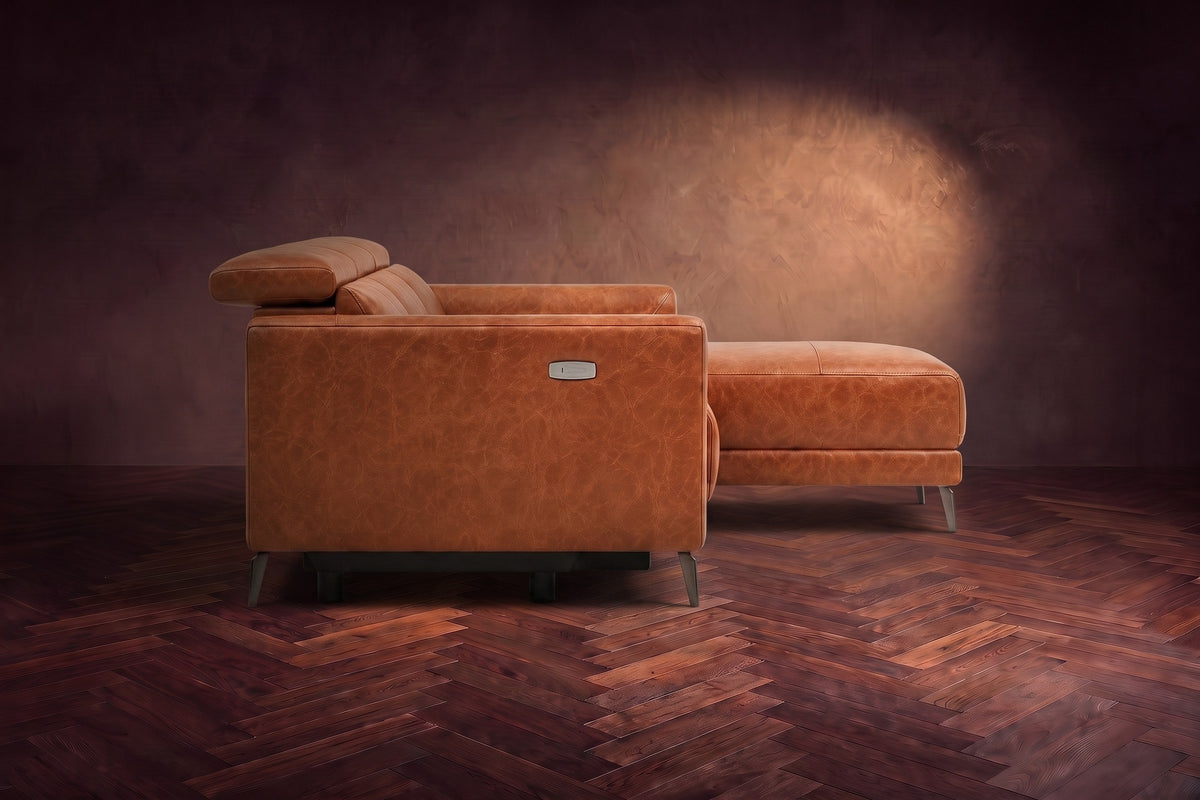 The Andria distressed leather sectional seen from its box-arm end, the chaise reaching forward, on a walnut herringbone floor. Shown in Tuscan Cognac, Right chaise.