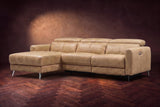 The Andria distressed Italian leather power reclining sectional on a walnut herringbone floor against a brown plaster wall, three-quarter view, headrests down and the footrest closed. Shown in Washed Sand, Left chaise.