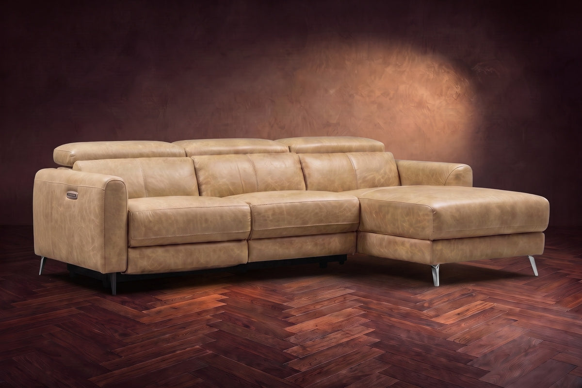 The Andria distressed Italian leather power reclining sectional on a walnut herringbone floor against a brown plaster wall, three-quarter view, headrests down and the footrest closed. Shown in Washed Sand, Right chaise.