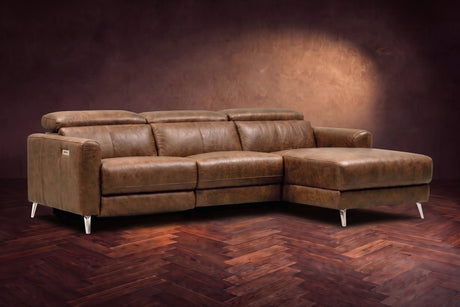 The Andria distressed Italian leather power reclining sectional on a walnut herringbone floor against a brown plaster wall, three-quarter view, headrests down and the footrest closed. Shown in Weathered Saddle, Right chaise.