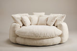 Aosta lounge chair in beige, straight front view: one thick round seat cushion inside a low channelled ring, square pillows along the back
