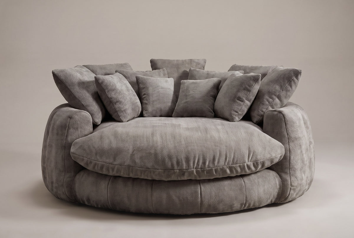 Aosta lounge chair in grey, straight front view: one thick round seat cushion inside a low channelled ring, square pillows along the back