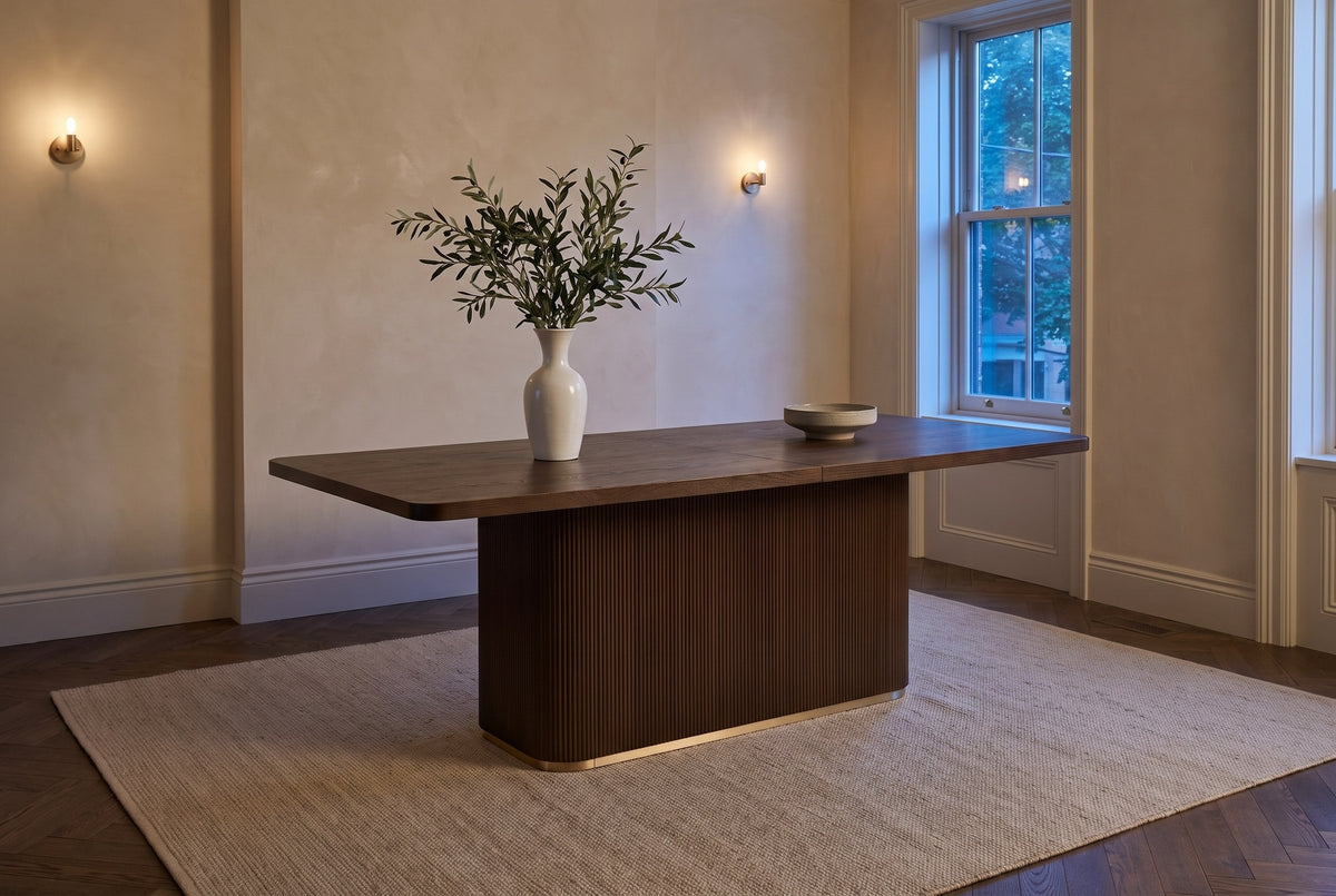 Aquileia dining table in a limewashed Toronto dining room at dusk, wall lights lit, olive branches in a white vase