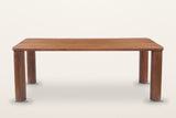 Arcevia dining table in Brown, straight front view on a warm white studio backdrop: a long slab top on four thick round legs