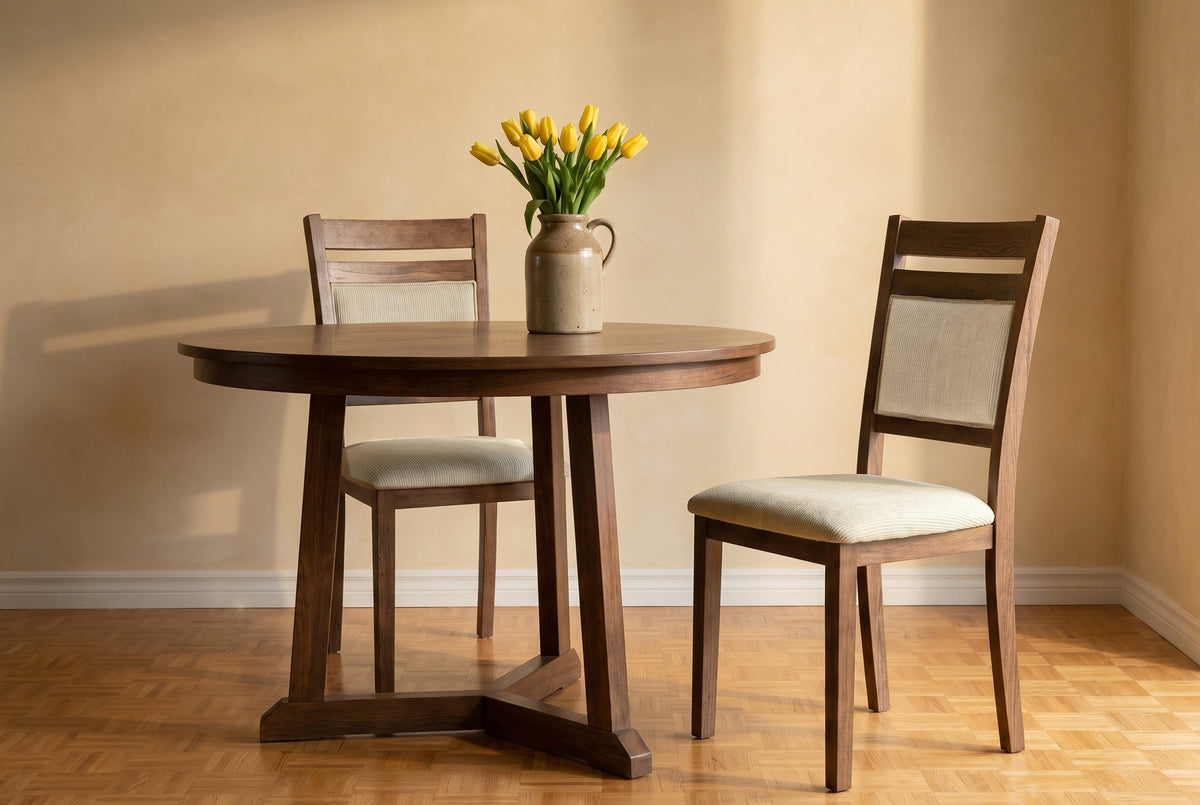 Two Arden dining chairs at a round walnut table with yellow tulips, one pulled out, against an ochre limewashed wall on an oak parquet floor