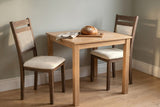 Two Arden dining chairs at a small oak table with a loaf on a board, against sage-grey walls in late sun