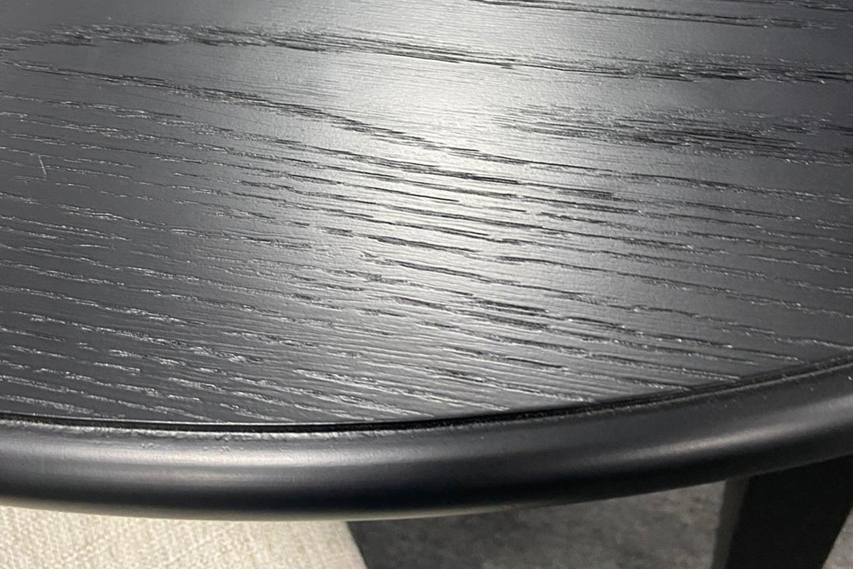Close-up of the Arden table in Black: the open oak grain under the black finish and the rounded moulded edge